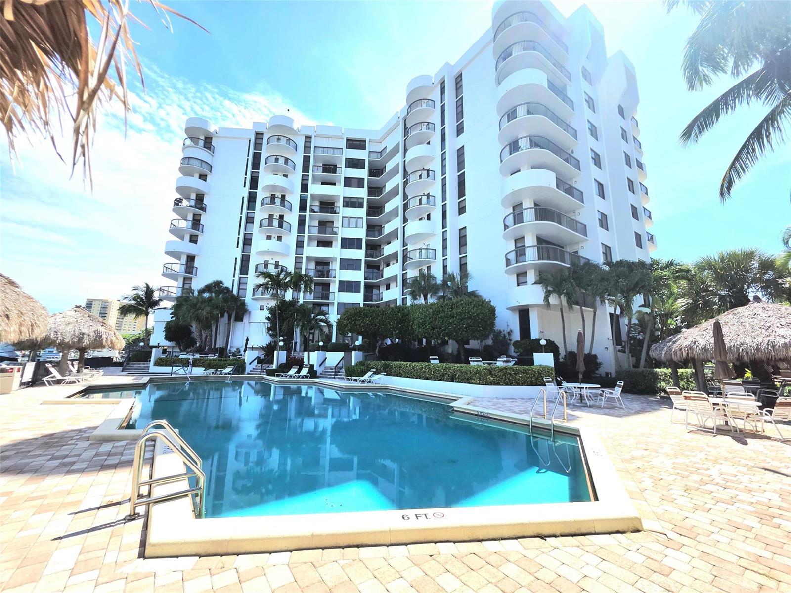 A swimming pool sits in front of a multi-story white residential building with curved balconies — 1631 S Ocean Boulevard # 1006, Pompano Beach FL 33062, POMPANO BEACH, FL
