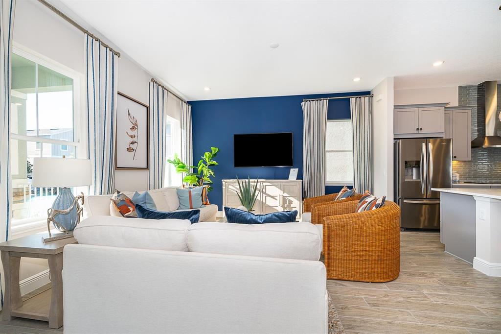 A living room features a blue accent wall, white sofa, wicker chairs, and adjacent kitchen — 13006 SERENE GLADE ROAD, WINTER GARDEN, FL