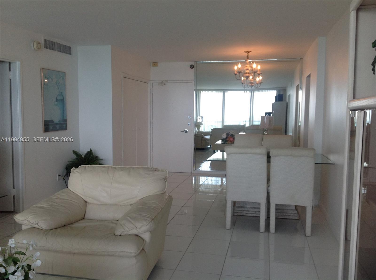 A living and dining area features white tile floors, a leather armchair, and a chandelier — 5151 Collins Ave # 1119, Miami Beach FL 33140, MIAMI BEACH, FL