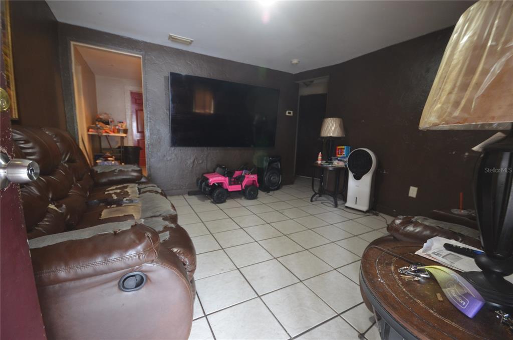 A living room features dark brown walls, a large wall-mounted television, and tiled flooring — 1607 E NOME STREET, TAMPA, FL