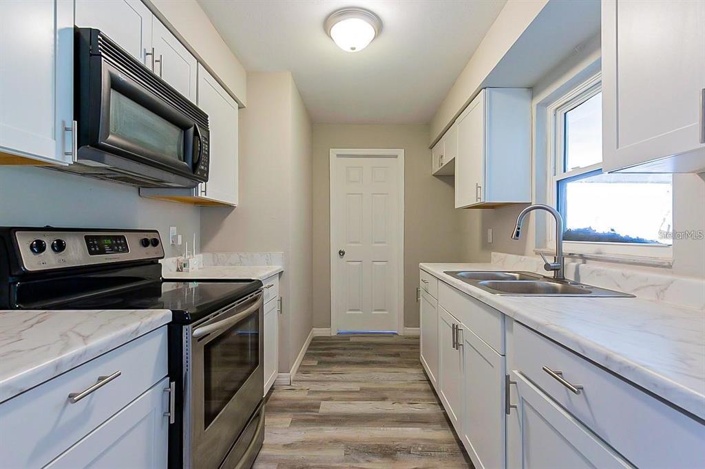 A galley-style kitchen features white cabinets, marble-look countertops, stainless steel appliances, and wood-look flooring — 3410 ALOHA DRIVE, SARASOTA, FL