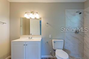 A bathroom features a white vanity, a mirror with a light fixture, and a tiled shower — 3410 ALOHA DRIVE, SARASOTA, FL