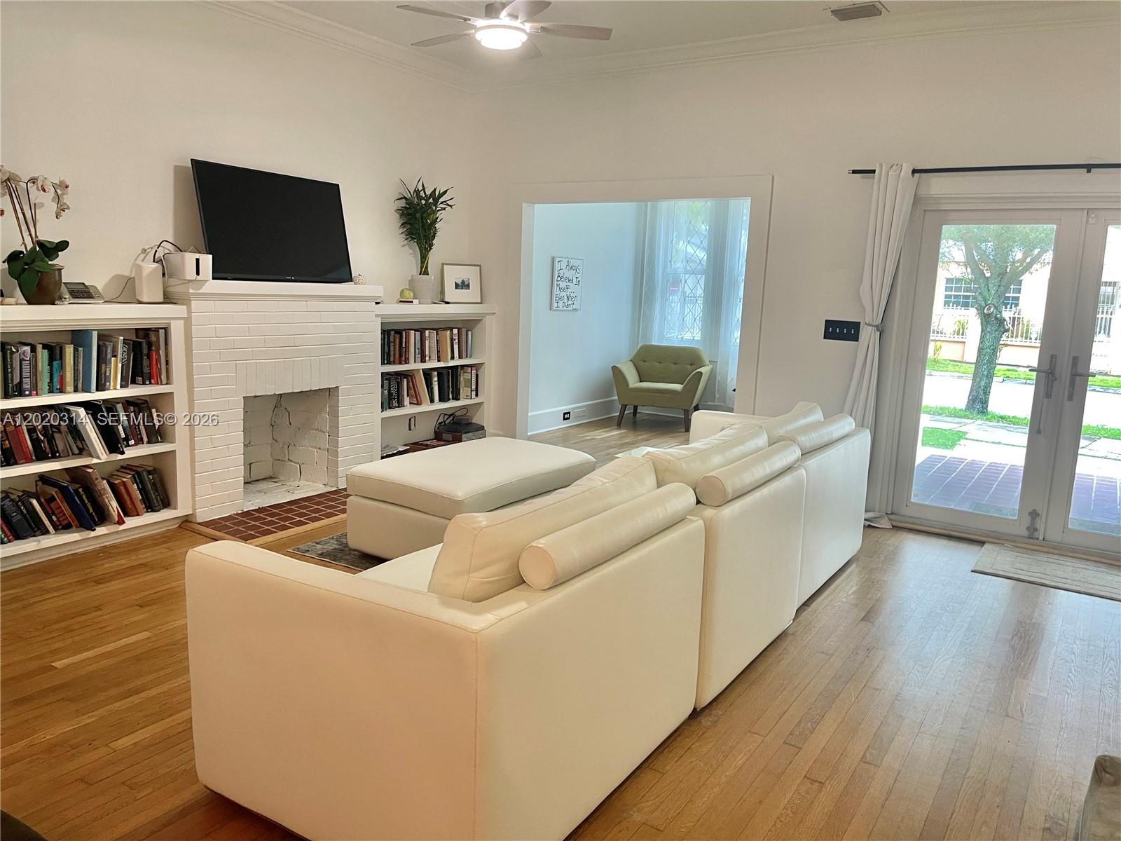 A living room features a white fireplace, built-in bookshelves, a white sofa, and hardwood floors — 27 NE 49th St, Miami FL 33137, MIAMI, FL