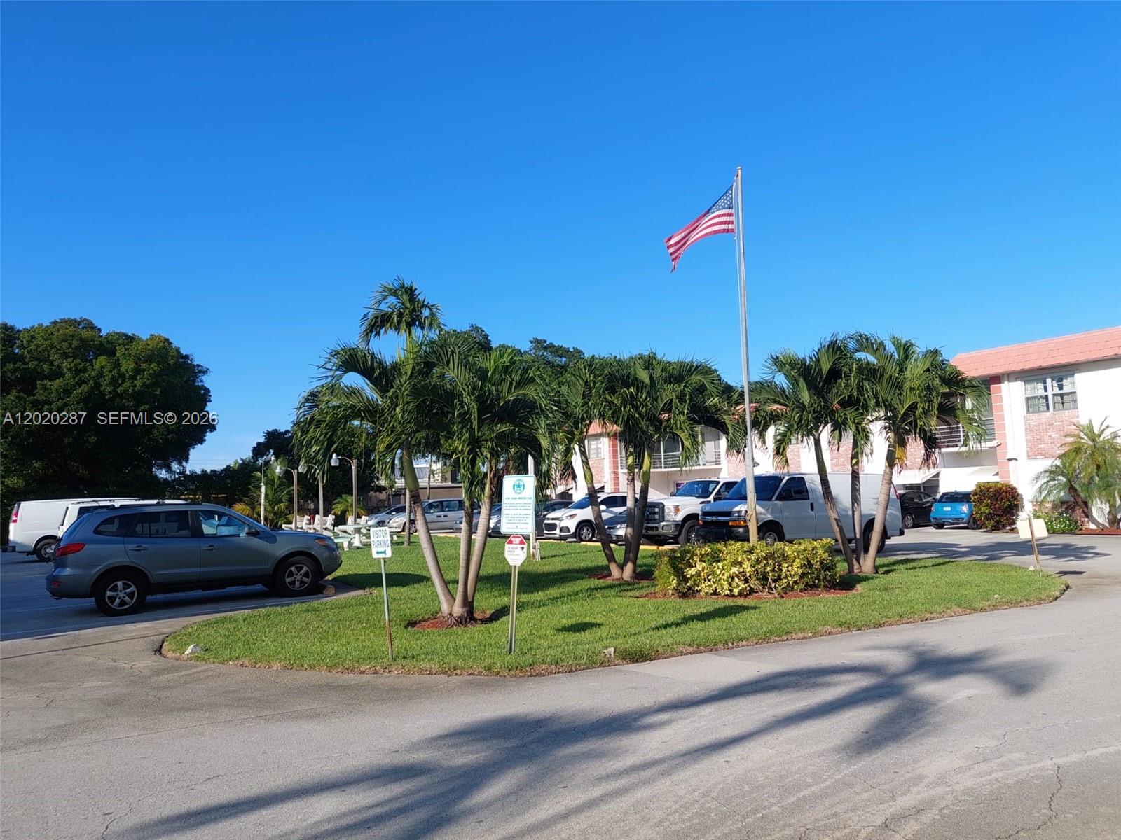 A parking lot with palm trees, a flag pole, and several vehicles in front of buildings — 3550 NW 8th Ave # 713, Pompano Beach FL 33064, POMPANO BEACH, FL