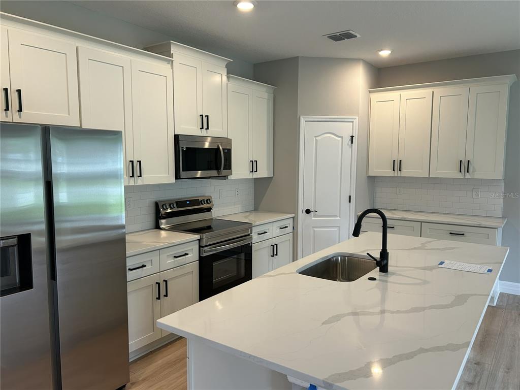 A modern kitchen features white cabinets, stainless steel appliances, and a large quartz-topped island — 15 LOBELIA COURT, HOMOSASSA, FL
