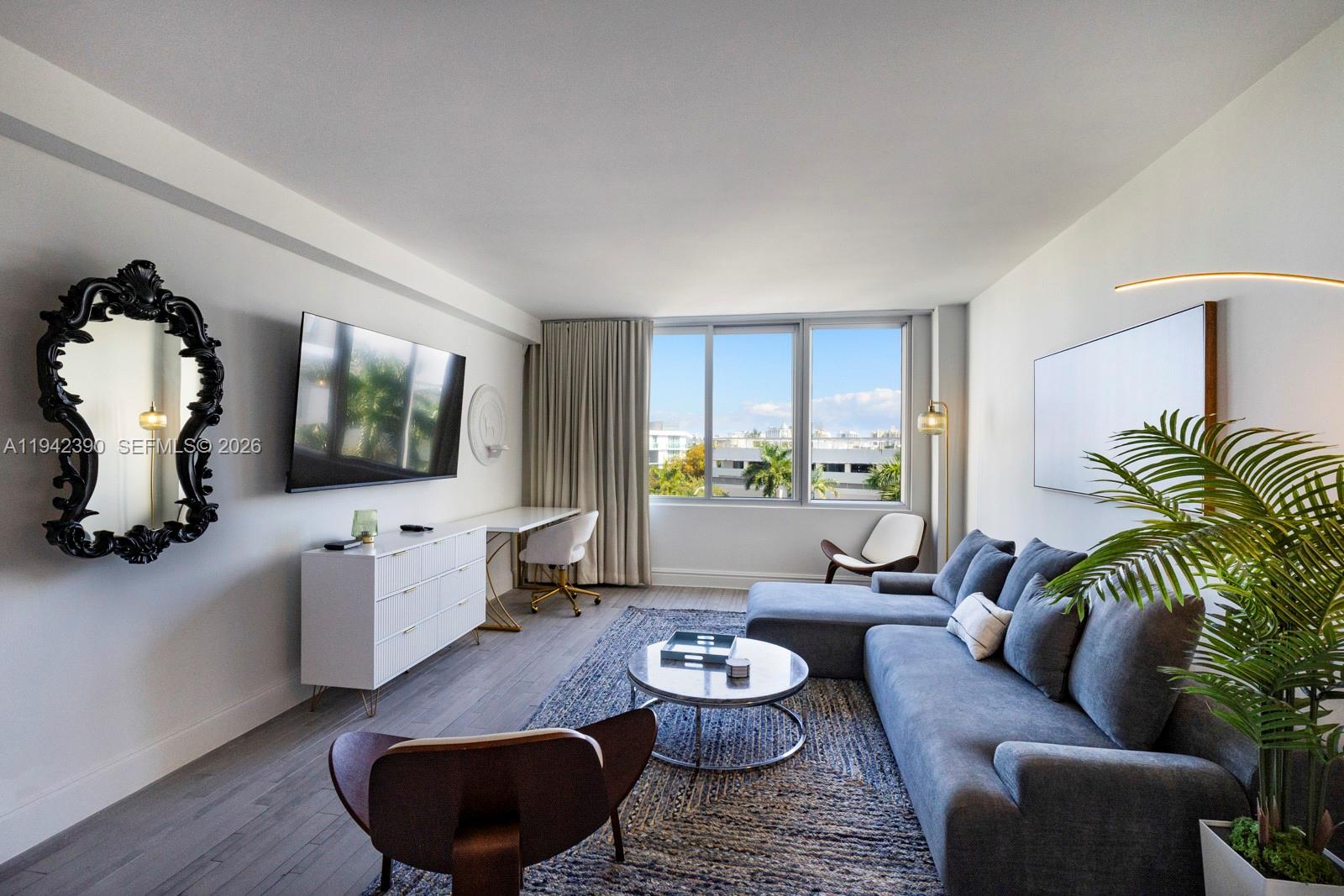 A modern living room features a grey sectional sofa, a white media console, and large windows — 1100 West Ave # 509, Miami Beach FL 33139, MIAMI BEACH, FL