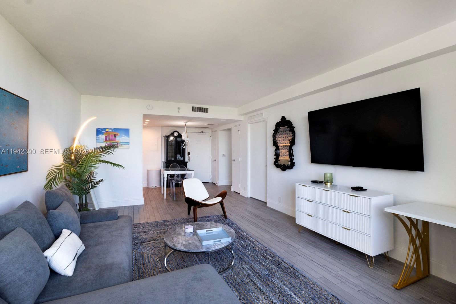 A living room features a grey sectional sofa, a white media console, and a dining area — 1100 West Ave # 509, Miami Beach FL 33139, MIAMI BEACH, FL