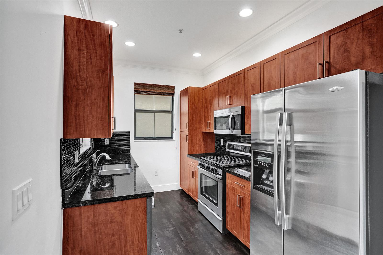 A kitchen features wood cabinets, stainless steel appliances, black countertops, and dark wood flooring — 12662 NW 32nd Place, Sunrise FL 33323, SUNRISE, FL