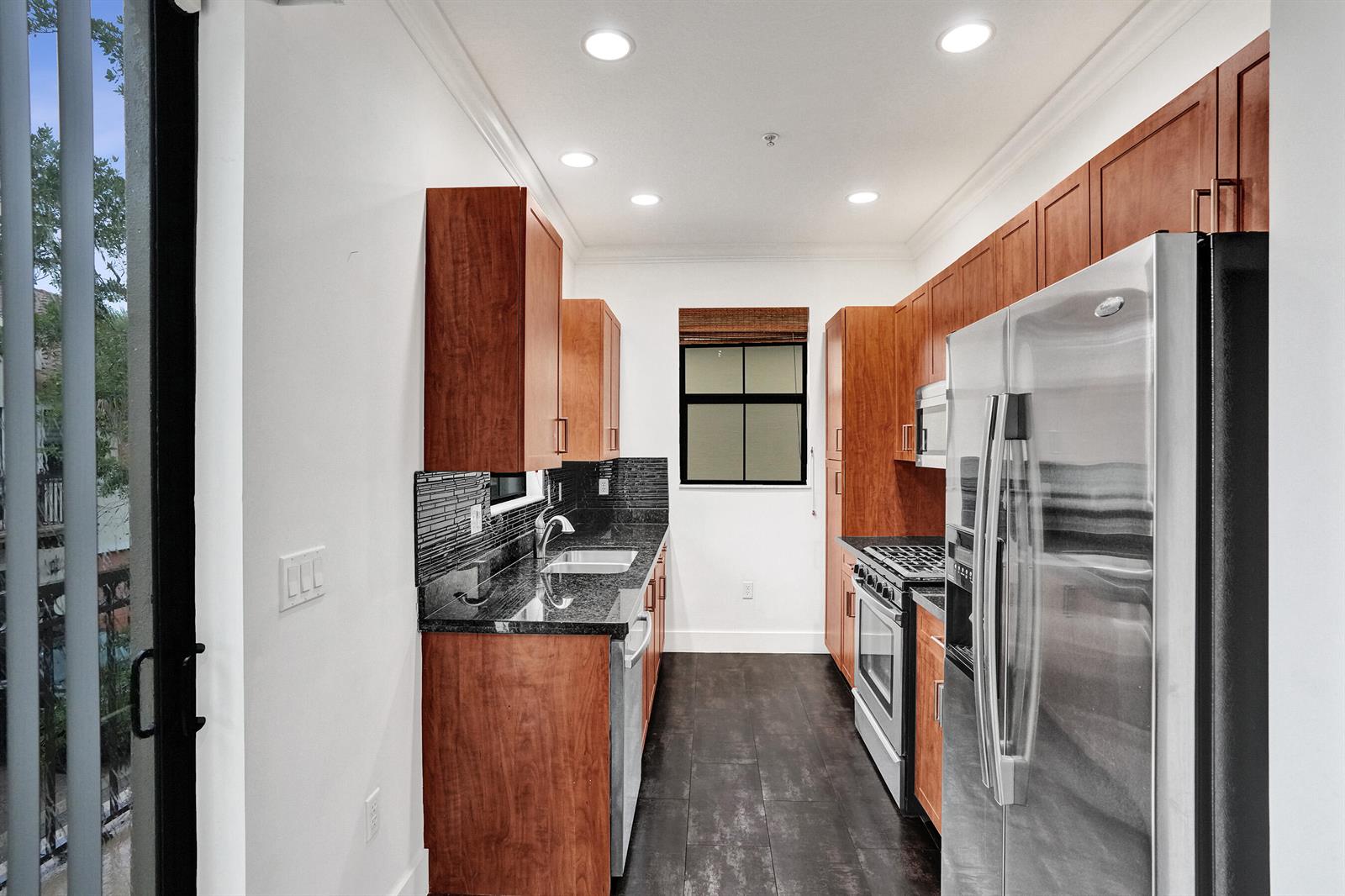 A galley kitchen features cherry wood cabinets, black granite countertops, and stainless steel appliances — 12662 NW 32nd Place, Sunrise FL 33323, SUNRISE, FL
