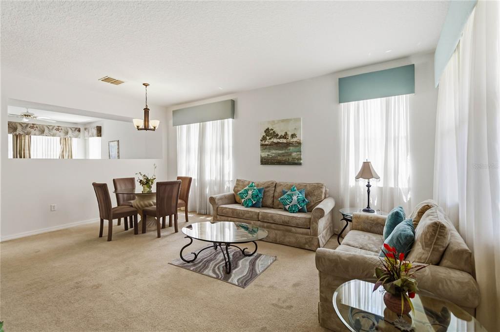 A living and dining area with beige carpet, two sofas, a glass coffee table, and chairs — 103 BAY LEAF LANE, DAVENPORT, FL
