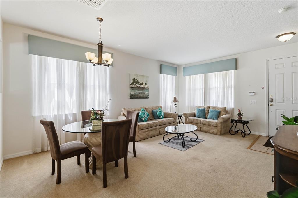 A combined dining and living area features beige carpeting, neutral walls, and light-colored furniture — 103 BAY LEAF LANE, DAVENPORT, FL