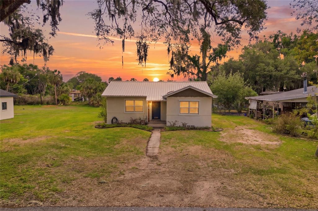 A single-story house with a metal roof sits on a grassy lot at sunset — 1570 IMPERIAL AVENUE, BARTOW, FL