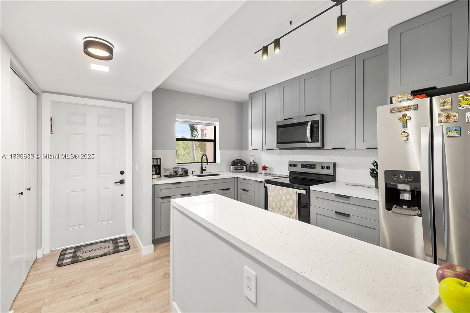 A kitchen features gray cabinets, white countertops, stainless steel appliances, and light wood-look flooring — 10444 NW 30th Ct # 202, Sunrise FL 33322, SUNRISE, FL