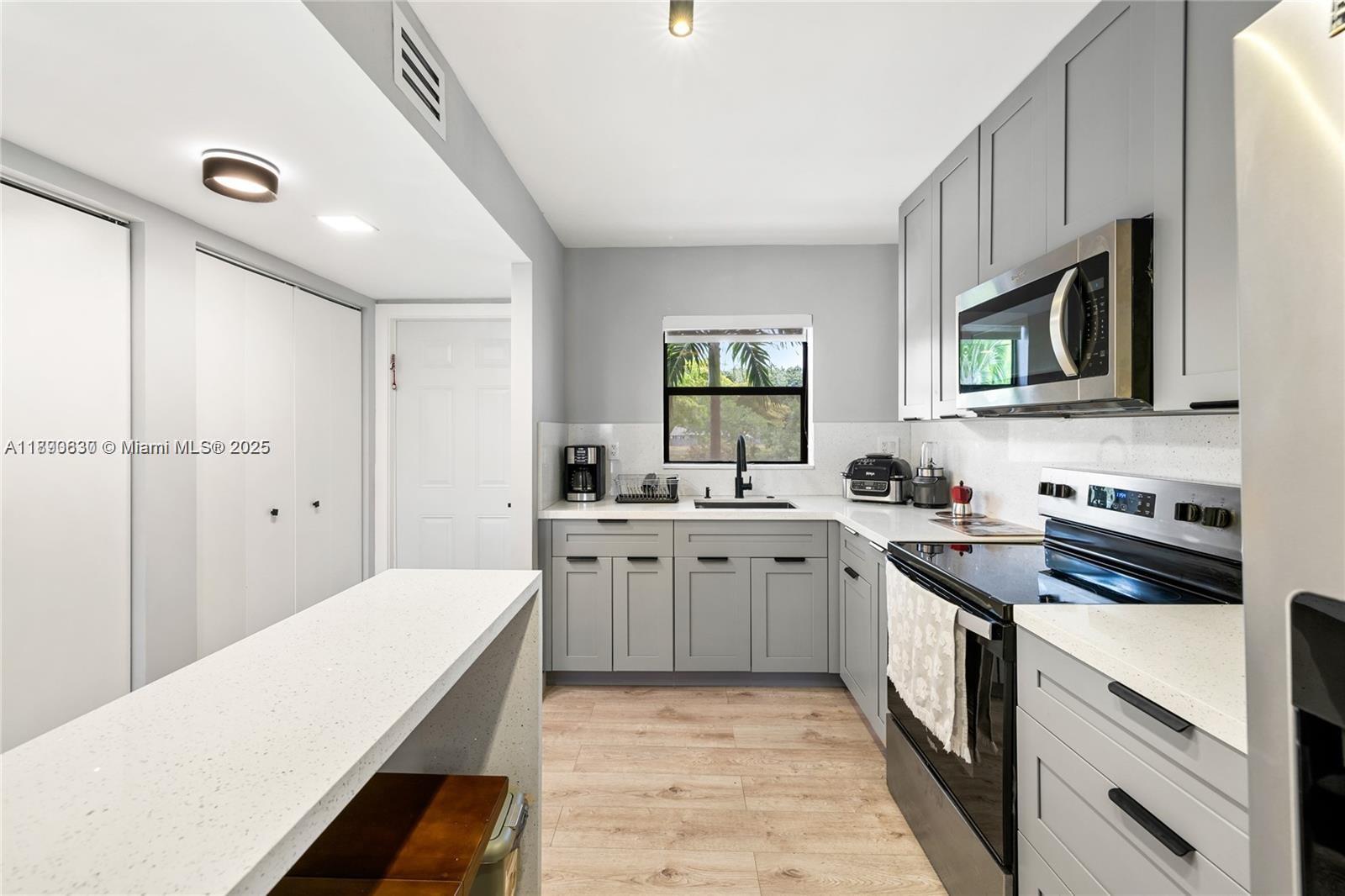 A kitchen features gray cabinets, white countertops, stainless steel appliances, and light wood flooring — 10444 NW 30th Ct # 202, Sunrise FL 33322, SUNRISE, FL