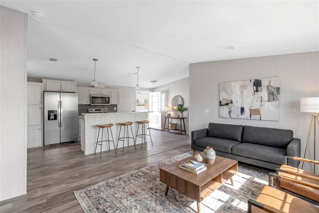 An open-concept living room and kitchen featuring wood-look flooring, a gray sofa, and bar seating — 2107 PALMA SOLA BOULEVARD UNIT 13, BRADENTON, FL