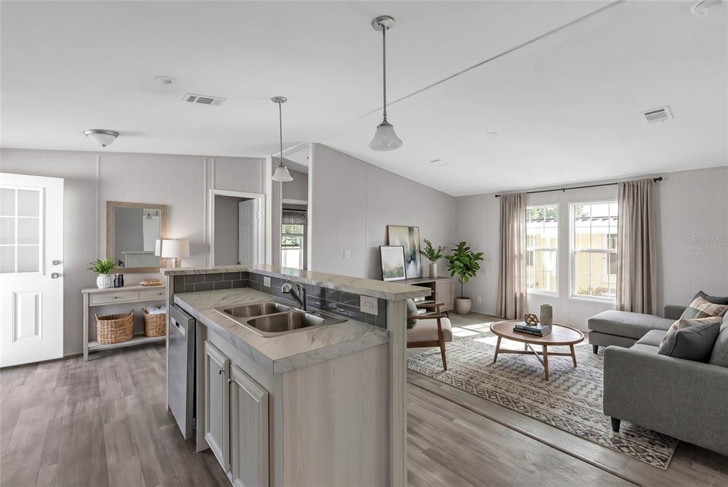 A kitchen with a sink island overlooks a living room with gray furniture and flooring — 2107 PALMA SOLA BOULEVARD UNIT 13, BRADENTON, FL