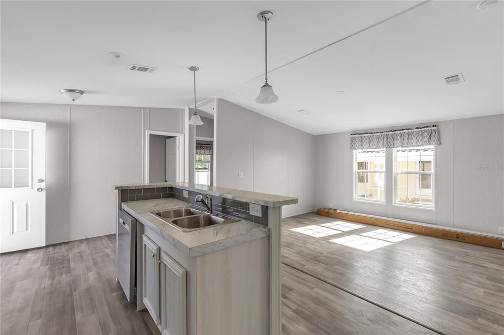 A kitchen island with a double sink overlooks an open-concept living area with wood flooring — 2107 PALMA SOLA BOULEVARD UNIT 13, BRADENTON, FL