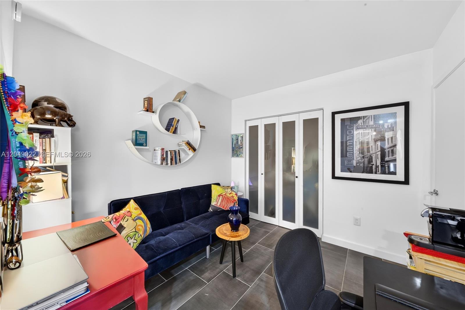 A home office features a dark blue sofa, a spiral wall shelf, and tiled flooring — 1100 S Miami Ave # 1603, Miami FL 33130, MIAMI, FL