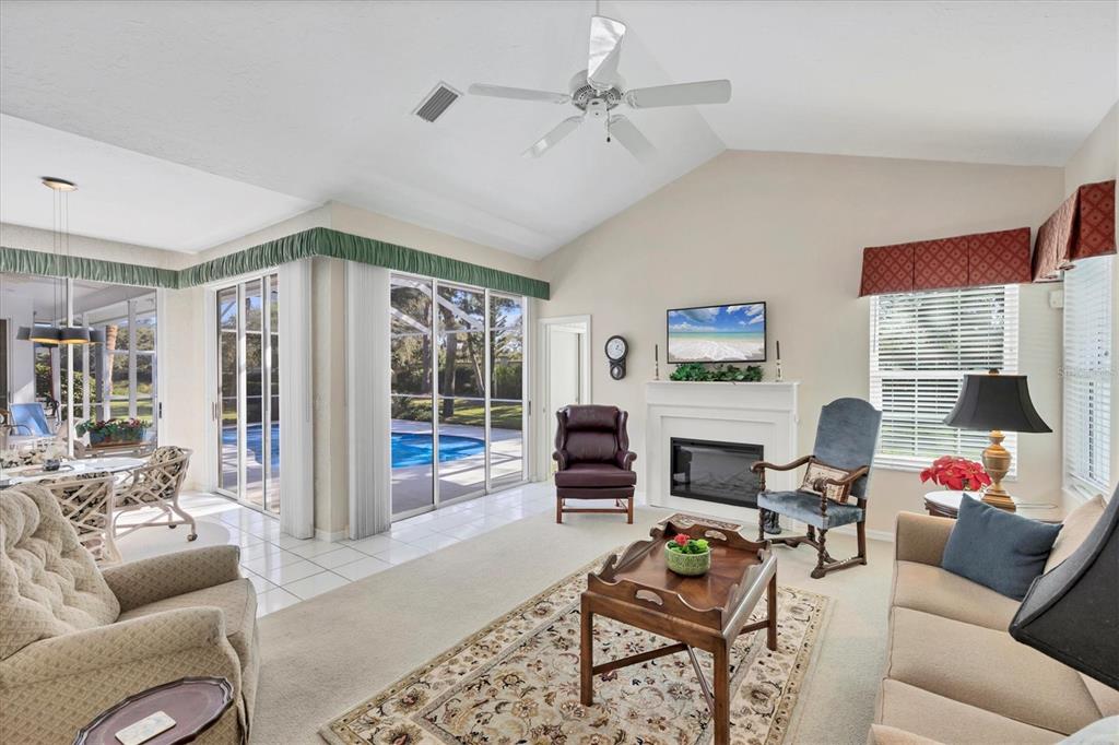 A living room with a fireplace, vaulted ceiling, carpeted floors, and sliding glass doors — 8684 WOODBRIAR DRIVE, SARASOTA, FL