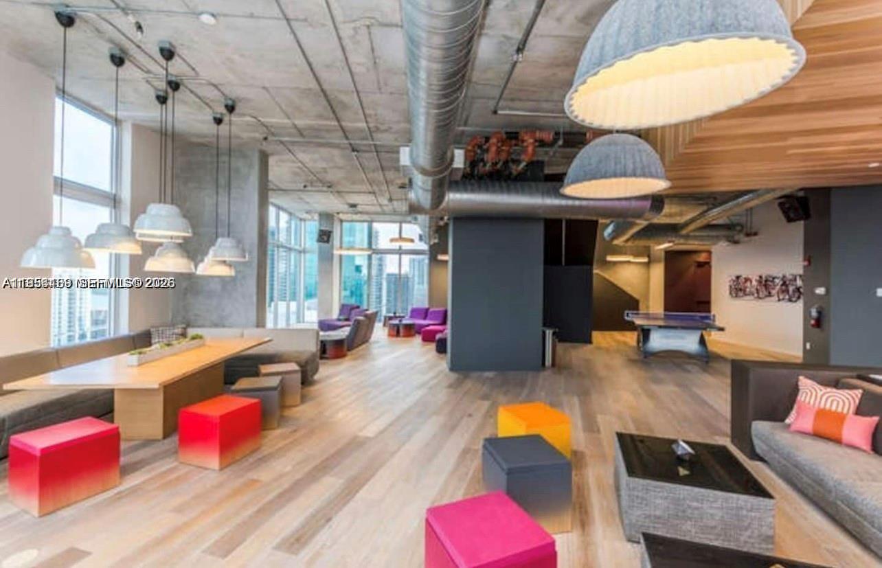 A modern, open-concept lounge features concrete ceilings, exposed ductwork, colorful cube seating, and a ping-pong table — 151 SE 1st St # 1207, Miami FL 33131, MIAMI, FL
