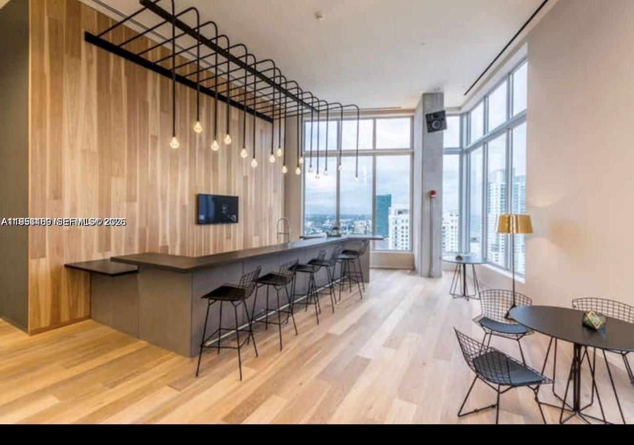 A modern bar area features a long counter, wood-paneled wall, and floor-to-ceiling windows — 151 SE 1st St # 1207, Miami FL 33131, MIAMI, FL