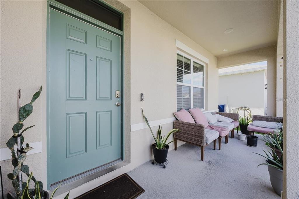A covered front porch features a light blue door, wicker seating, and several potted plants — 344 ALEXZANDER WAY, WINTER HAVEN, FL
