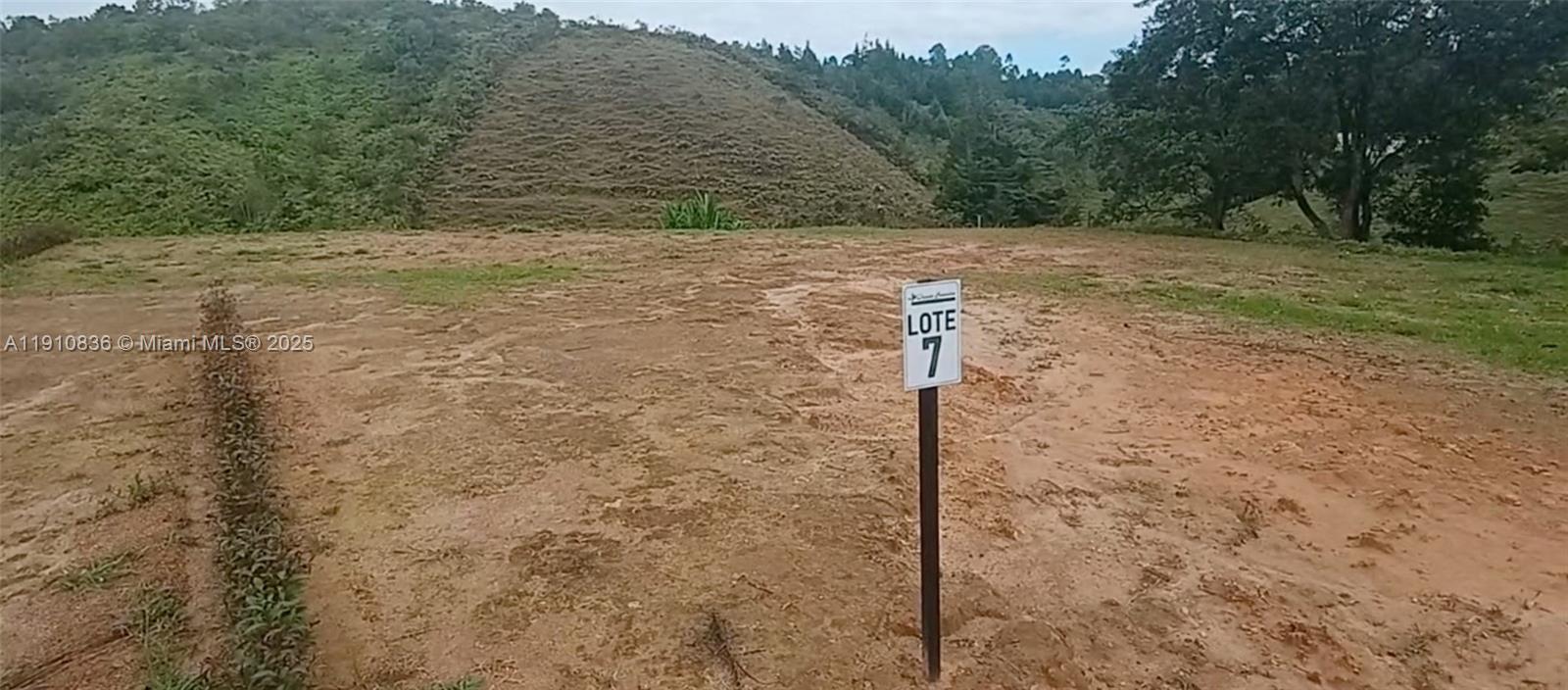 A sign labeled Lote 7 stands on a cleared, dirt plot of land with hills — Vereda Mampuesto Sector Garrido #7, C Colombia, C