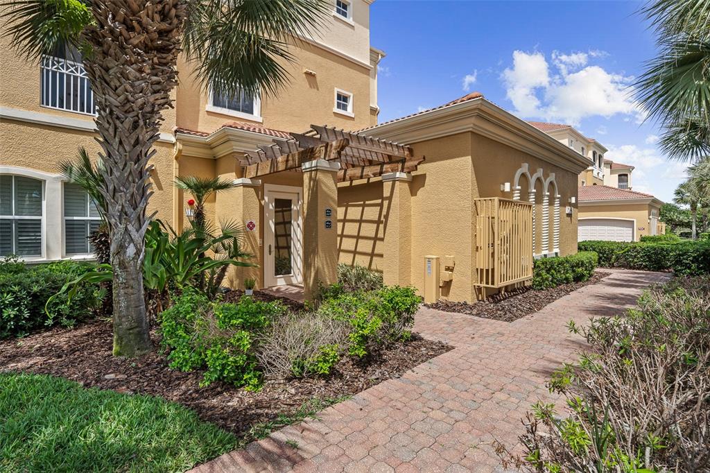 An exterior view of a tan stucco building with a pergola over the front entrance — 165 AVENUE DE LA MER UNIT 402, PALM COAST, FL