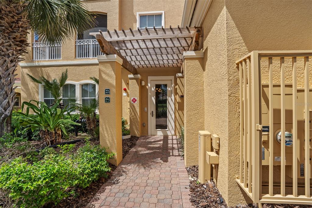A paved walkway leads to the entrance of a tan stucco building with a pergola — 165 AVENUE DE LA MER UNIT 402, PALM COAST, FL