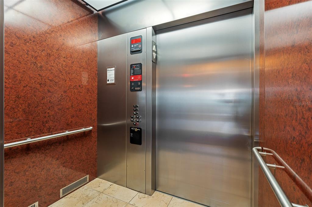 An elevator interior features wood-patterned walls, stainless steel doors, and a metal control panel — 165 AVENUE DE LA MER UNIT 402, PALM COAST, FL