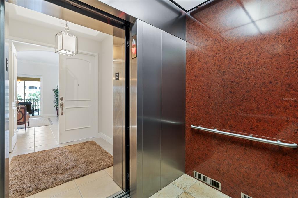 An elevator opens into a tiled foyer with a white door and a brown rug — 165 AVENUE DE LA MER UNIT 402, PALM COAST, FL
