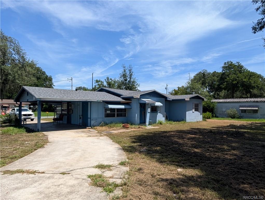 A single-story blue house with a carport and a concrete driveway under a blue sky — 716 S EDEN GARDENS AVENUE, INVERNESS, FL