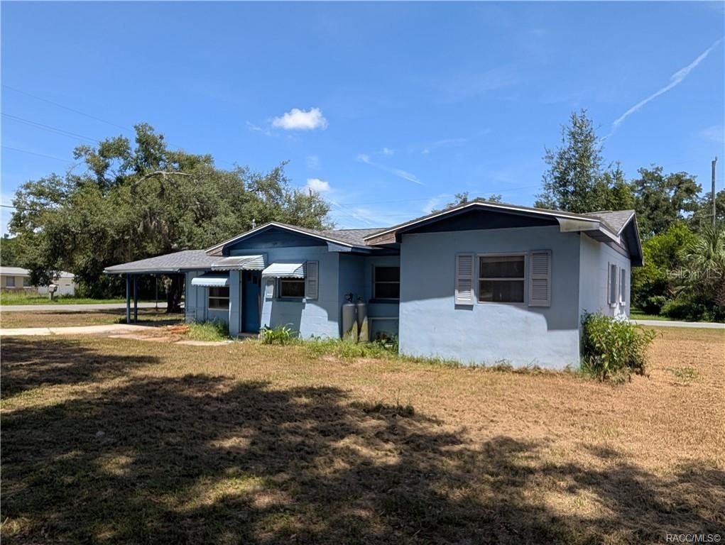 A light blue, single-story house with a carport and metal awnings under a blue sky — 716 S EDEN GARDENS AVENUE, INVERNESS, FL