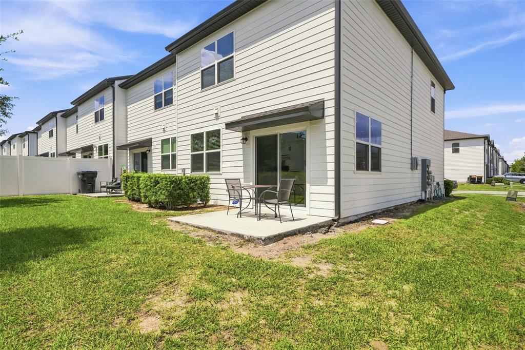 The exterior of a two-story townhouse features light siding, a concrete patio, and a lawn — 645 MADISON DRIVE, DAVENPORT, FL