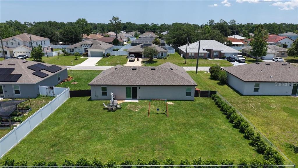 An aerial view shows the backyard of a single-story house with a lawn and fence — 26 ROCKINGHAM LANE, PALM COAST, FL