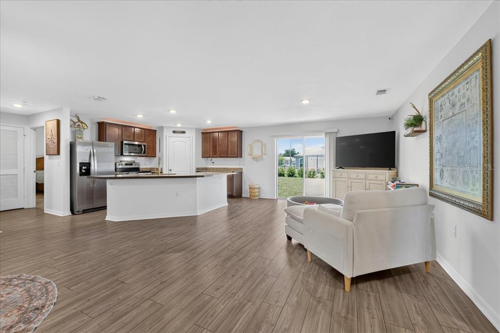 An open-concept kitchen and living area features wood-look flooring, white cabinetry, and a sliding door — 26 ROCKINGHAM LANE, PALM COAST, FL