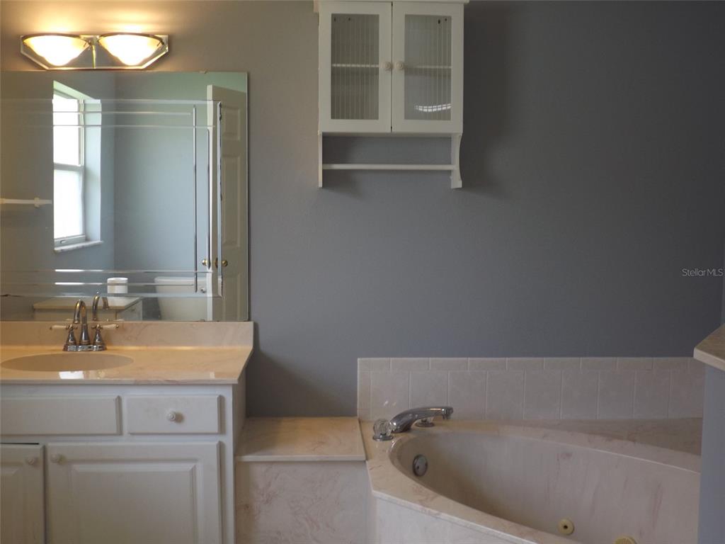 A bathroom features a white vanity with a marble countertop, a soaking tub, and wall cabinet — 9 BOWMAN PLACE, PALM COAST, FL