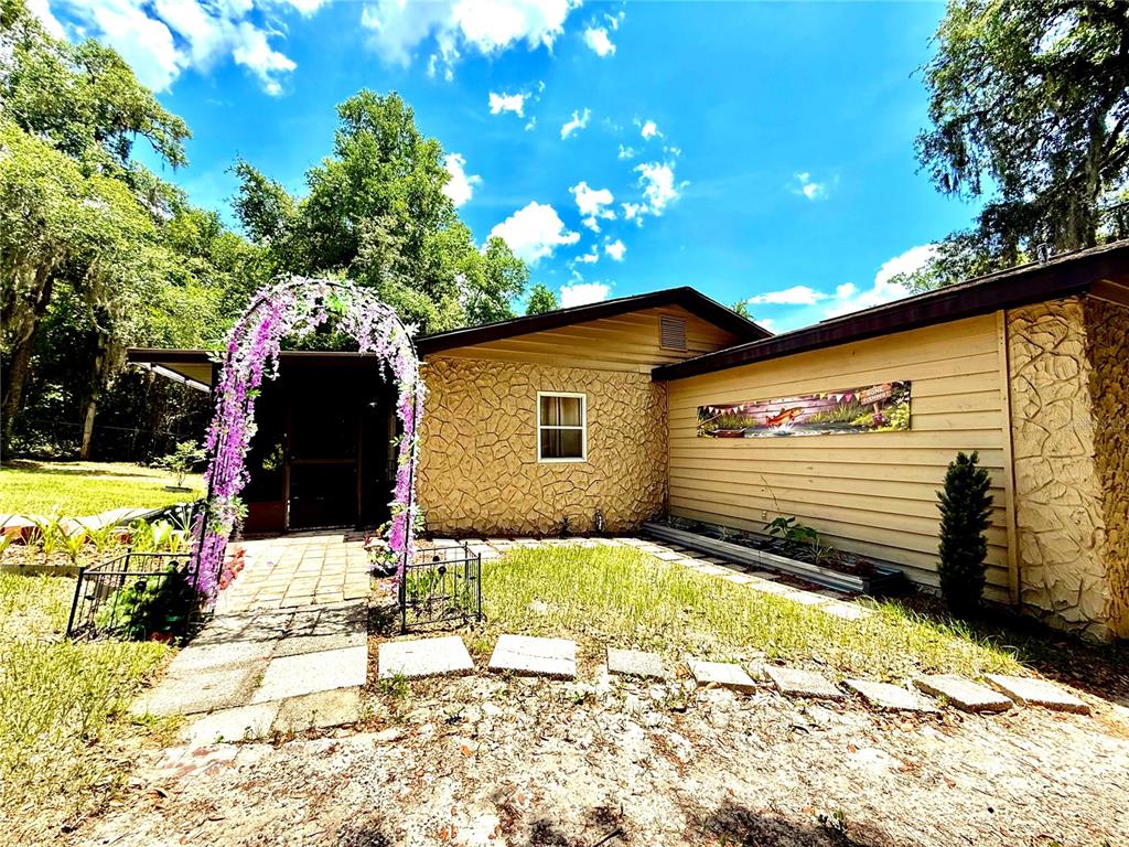 A single-story house exterior features stone siding, a purple floral archway, and a paved walkway — 208 ASHLEY STREET, HAWTHORNE, FL