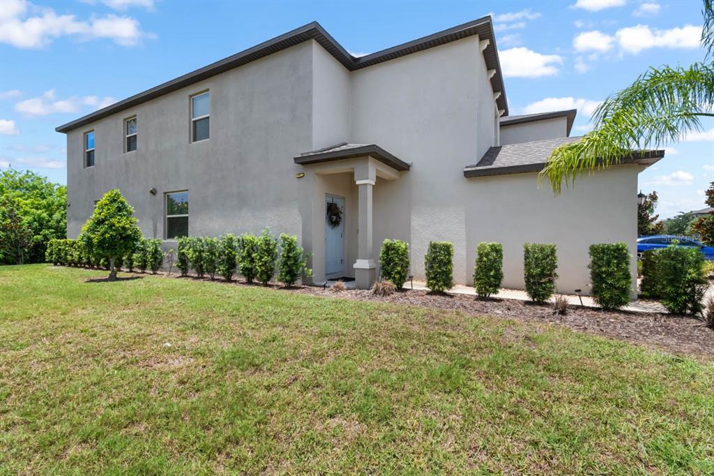A two-story house exterior with a light-colored stucco facade, a covered entryway, and manicured shrubs — 635 ROYAL EMPRESS DRIVE, RUSKIN, FL