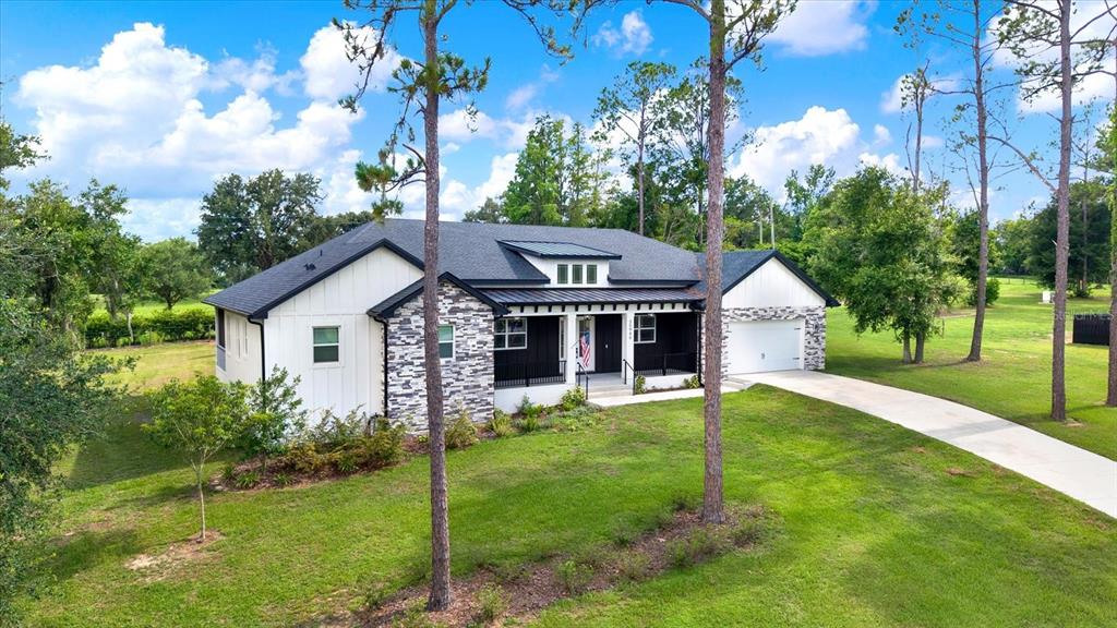 A modern farmhouse with white vertical siding, stone accents, and a dark metal roof — 35940 RAMSEY RIDGE DRIVE, DADE CITY, FL