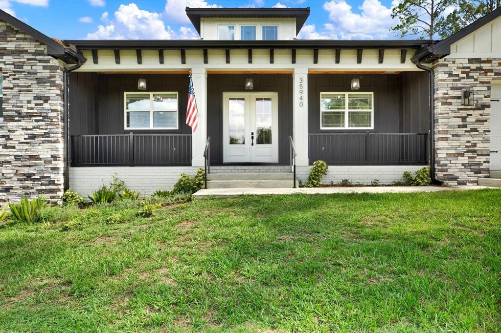 A front view of a house with a covered porch, stone siding, and dark trim — 35940 RAMSEY RIDGE DRIVE, DADE CITY, FL