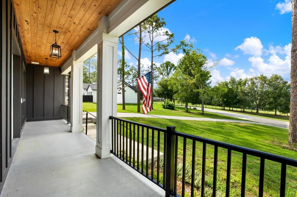 A covered front porch with a wood-paneled ceiling, black railings, and a view of grass — 35940 RAMSEY RIDGE DRIVE, DADE CITY, FL