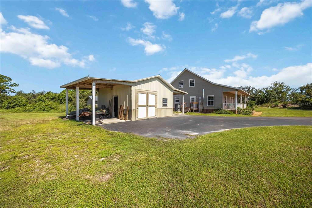 A detached metal garage with an open carport sits beside a two-story house — 2711 SNYDER ROAD, SEBRING, FL