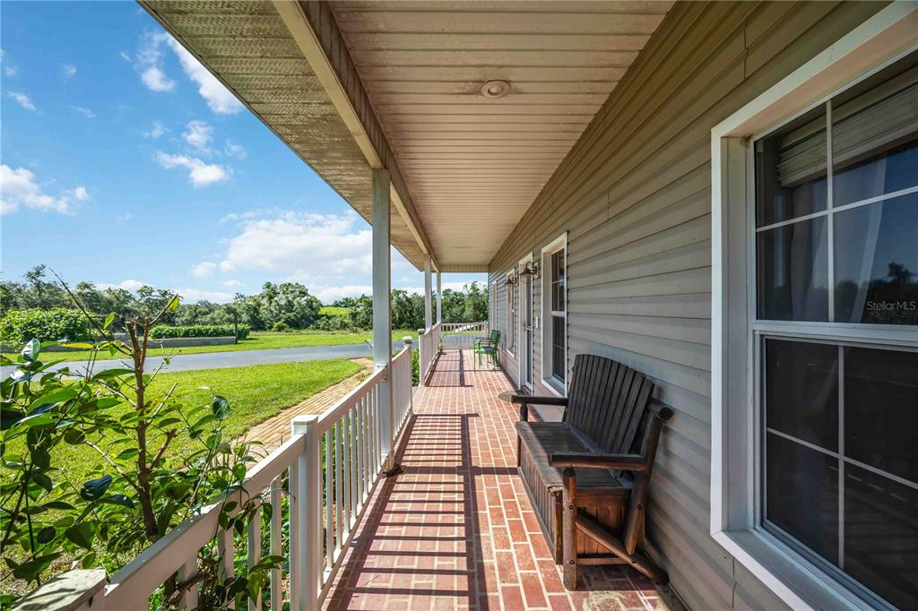 A covered porch with a brick floor, white railing, and a wooden bench — 2711 SNYDER ROAD, SEBRING, FL