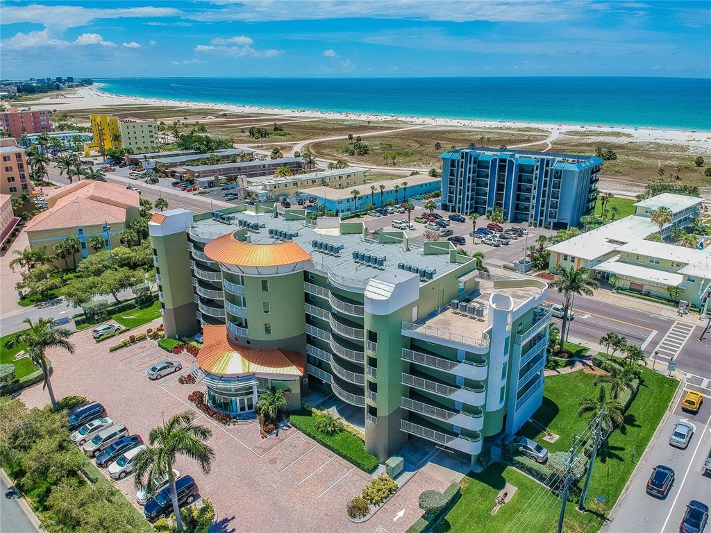 An aerial view of a multi-story green hotel building near a sandy beach and ocean — 11605 GULF BOULEVARD UNIT 402, TREASURE ISLAND, FL
