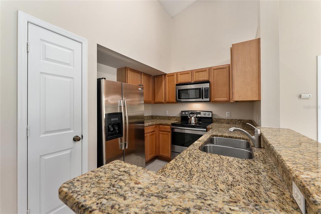 A kitchen features wood cabinets, granite countertops, stainless steel appliances, and a vaulted ceiling — 10000 SW 52ND AVENUE UNIT 42, GAINESVILLE, FL