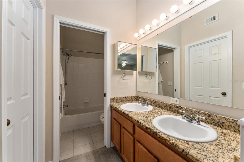 A bathroom features a double vanity with granite countertops, wood cabinets, and a shower-tub combo — 10000 SW 52ND AVENUE UNIT 42, GAINESVILLE, FL
