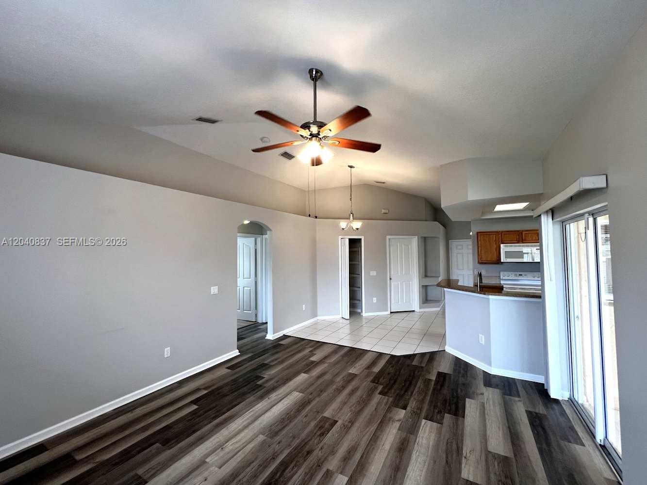 A living room with wood-look flooring transitions into a tiled dining area and kitchen — PORT ST. LUCIE, FL