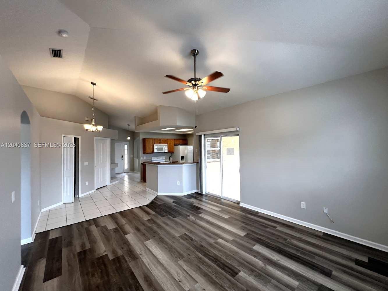 A living room with wood-look flooring transitions to a tiled kitchen area with a breakfast bar — PORT ST. LUCIE, FL