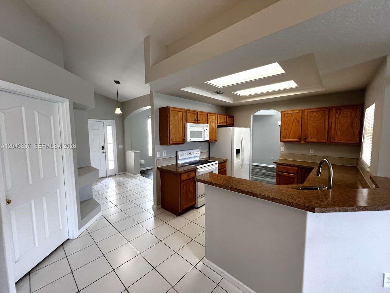 A kitchen features wood cabinets, granite-look countertops, white appliances, and white tile flooring — PORT ST. LUCIE, FL